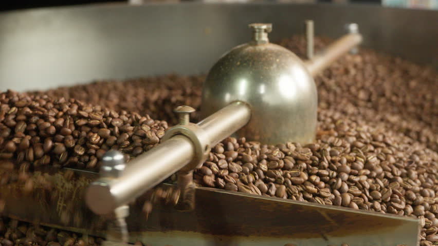 Close up roasted coffee beans mixing in mixer roaster blend automatic metal drum machine stirring roasting cocoa caffeine at production facility aromatic grains in grinder industrial food preparation