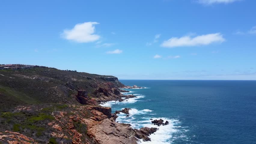 Rocky cliffs and rugged shoreline meet the waters of the Southern Ocean near Mossel Bay, South Africa, with waves breaking along the exposed coast.