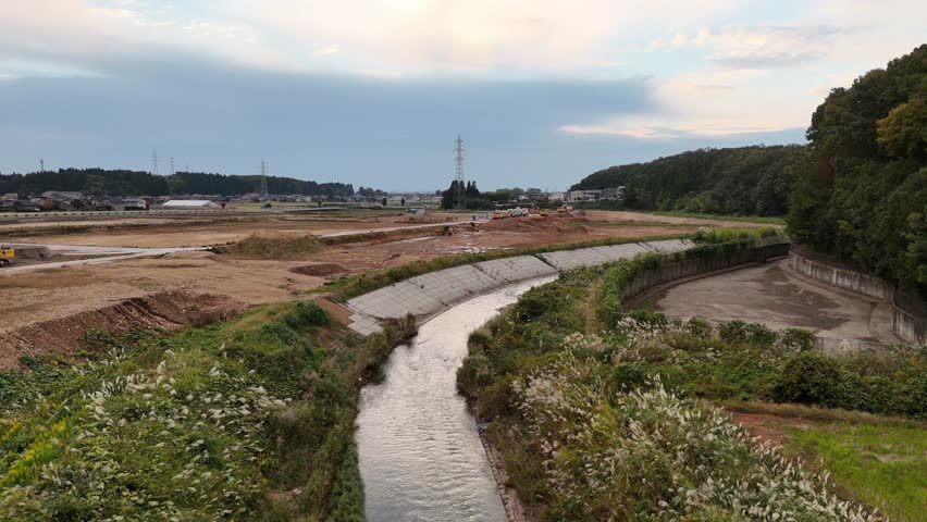 A river with a green and brown landscape. The water is calm and the sky is cloudy. The scene is peaceful and serene