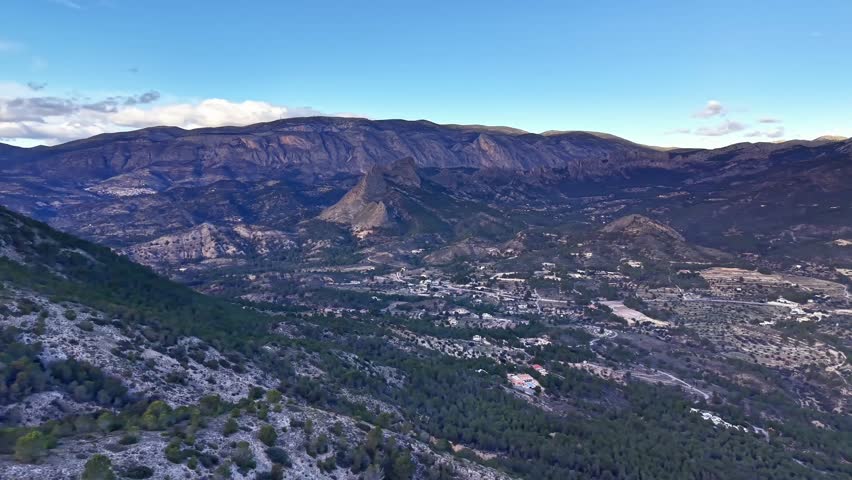sunlit ridge overlooking sprawling valley and distant plateau with scattered settlements energetic trail