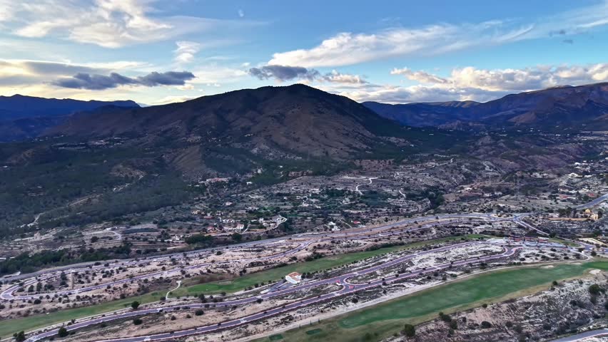 Cinematic valley view with river slicing through town, evening light casting silhouettes on ridgelines, busy