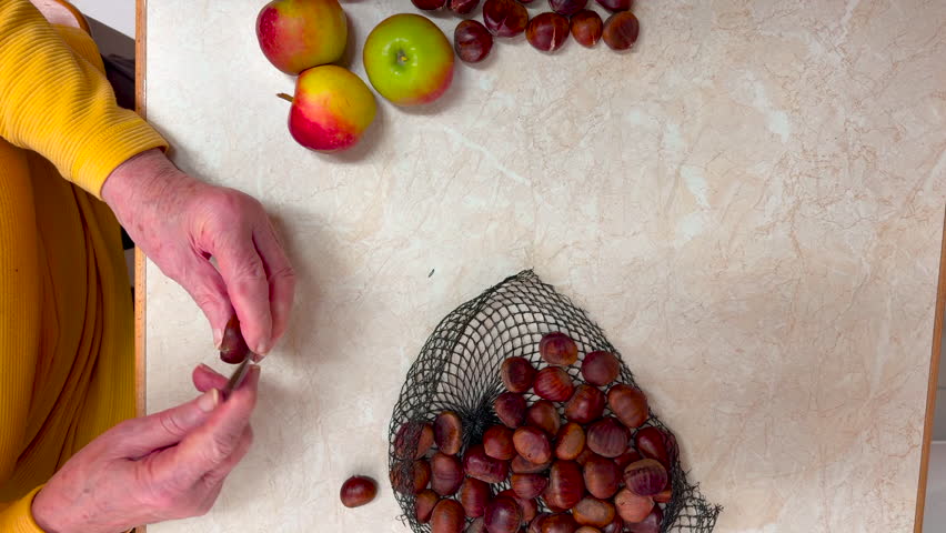 A housewife sorts chestnuts, cutting them crosswise, apple are laying on the table, static shot