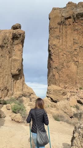 Roque Nublo: Hiker walking on a mountain trail towards a gap between two giant volcanic rock formations. Gran Canaria.