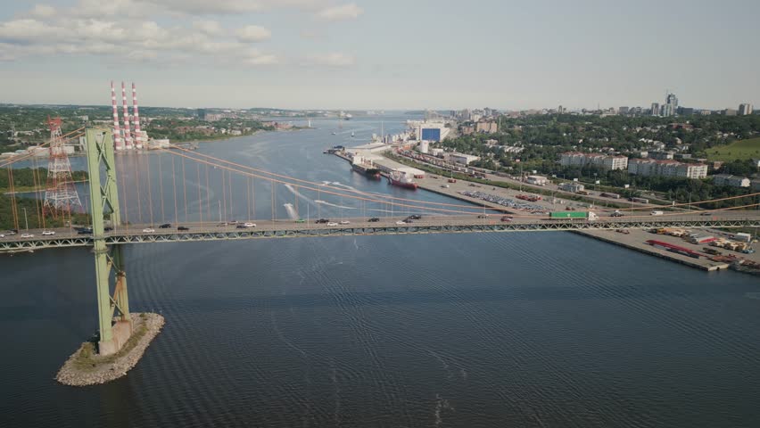 Aerial Footage Shows The Mackay Bridge In Nova Scotia Canada With Bright Sunshine Blue Skies And Cars Moving Across The Structure Connecting Halifax And Dartmouth Over Sparkling Harbor Water