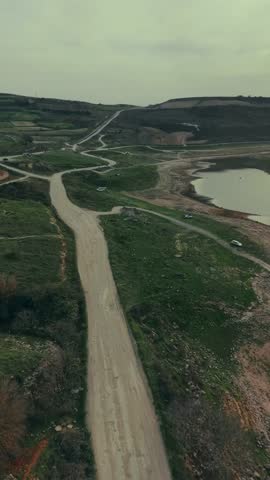 An aerial view of winding rural roads cutting through green fields and rolling hills, showcasing a quiet countryside landscape with scattered paths, farmland patches, and a sense of openness and journ