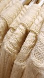 Cream-colored cable knit sweaters hang in a row on hangers. Close-up shot reveals the soft, fuzzy texture and intricate knit pattern as the camera slowly pans. - Powered by Shutterstock - Get 15% off with code: PIKWIZARD15