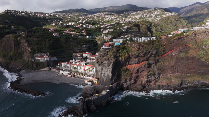 Overcast mountain settlement beside turbulent ocean with white houses