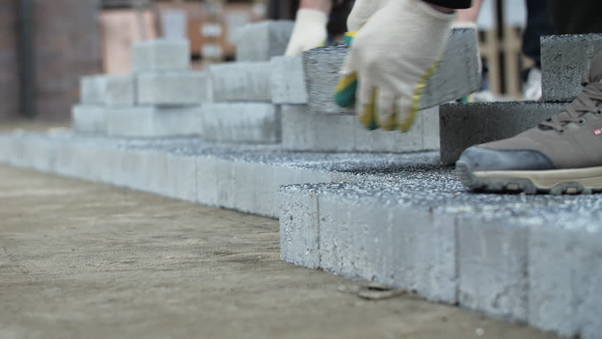 Worker laying sidewalk paving stone layer by hand