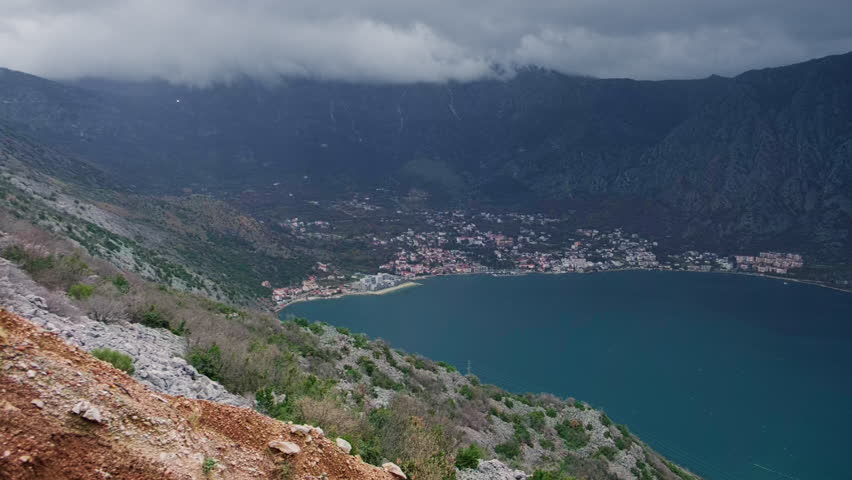 Panoramic view of deep blue bay, framed by steep mountains under heavy dramatic clouds. Rugged terrain of Adriatic sea coastline in Kotor Bay, Montenegro