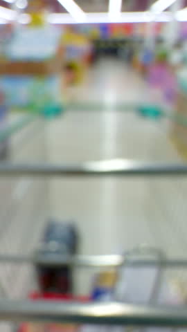 First-Person View Through an Empty Shopping Cart Moving Down a Bright Supermarket Aisle, Colorful Shelves Out of Focus, Consumerism Concept.