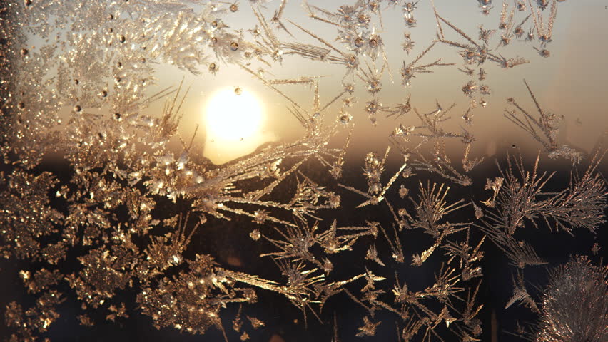 Beautiful frost patterns on glass against cityscape and rising sun. Needle like tree shaped crystals and dendrites of frozen moisture on window. Scenic real background and panning in winter.