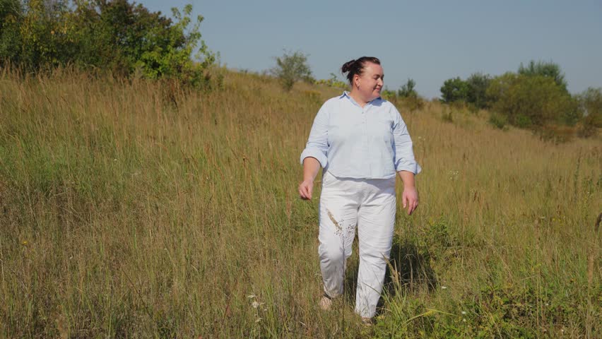 Confident plus-size woman walking through a sunny field with tall grass on a summer day