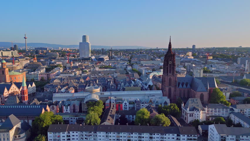 Aerial drone view from 100m over the Main River to Frankfurt Cathedral. Scenic flight showing the historic Kaiserdom church with the modern city skyline and skyscrapers in Frankfurt am Main, Germany.