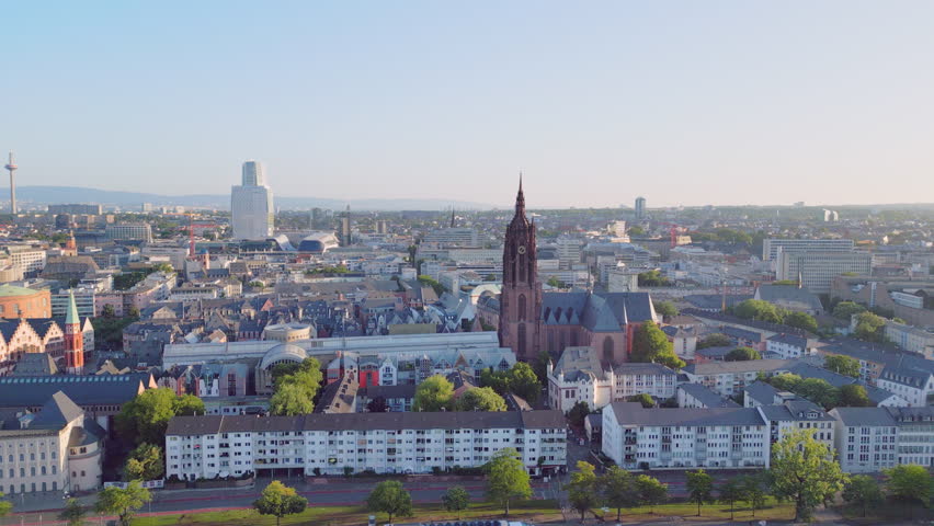 Aerial drone view from 100m over the Main River to Frankfurt Cathedral. Scenic flight showing the historic Kaiserdom church with the modern city skyline and skyscrapers in Frankfurt am Main, Germany.