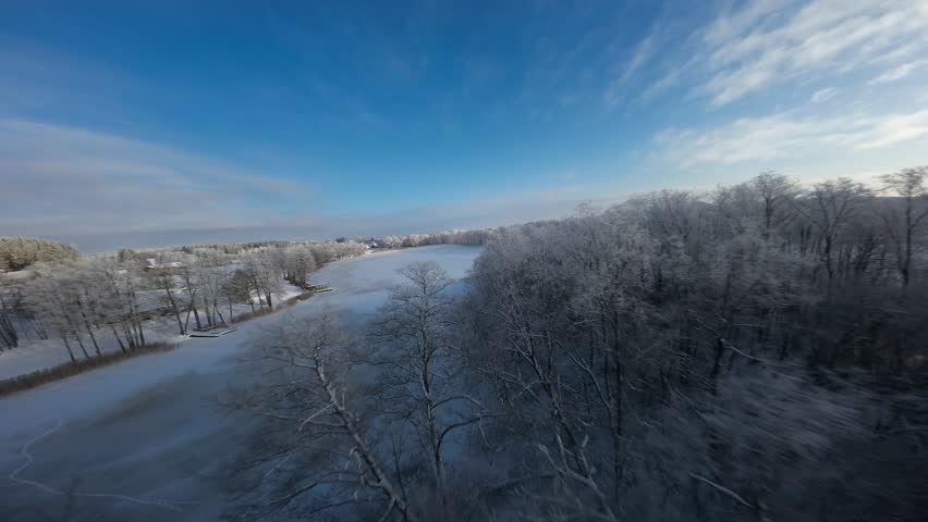 Fast FPV drone flight sweeping over a snow-covered frozen field and frosty trees under a bright blue sky. High-speed motion with long shadows and crisp winter atmosphere.