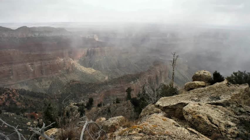 Cinematic 4K aerial footage captures the majestic Grand Canyon shrouded in ethereal mist. Dramatic layered rock formations under a soft, diffused light, evoking awe and natural wonder.
