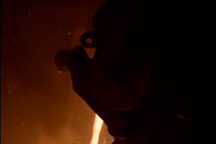 Steel works in Nizhny-Tagil, Russia. Dark silhouette of open hearth ladle in foreground, MS orange glowing molten iron pours from ladle amid orange smoke and flames.