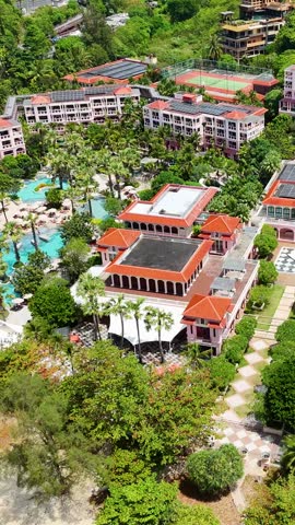 Drone footage showing a luxury resort with red roofs, lush greenery, and sandy beach.