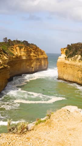 A vertical perspective of majestic limestone cliffs surrounding a turquoise ocean inlet under bright daylight.