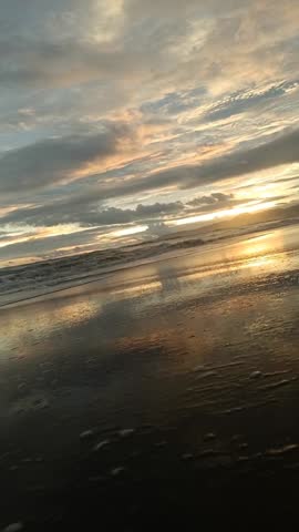 Golden hour sunset over a tropical beach with dramatic clouds reflecting on the wet sand at low tide.