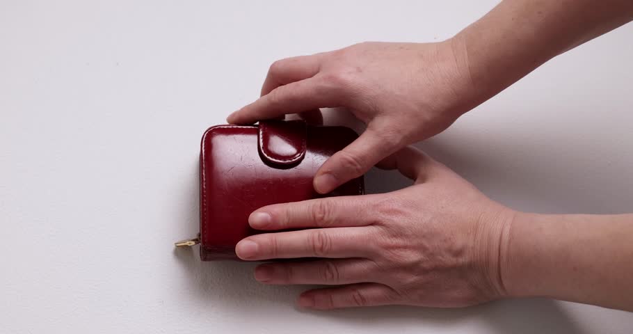 Person opens a small, shiny, red wallet on a white table. Inside, it is mostly empty with only a few coins. The wallet is then closed and rests on the table.