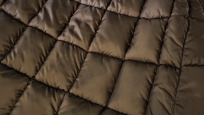 A woman presses her index finger on a quilted fabric for a down jacket. Black lining with polyester for sewing warm clothes.