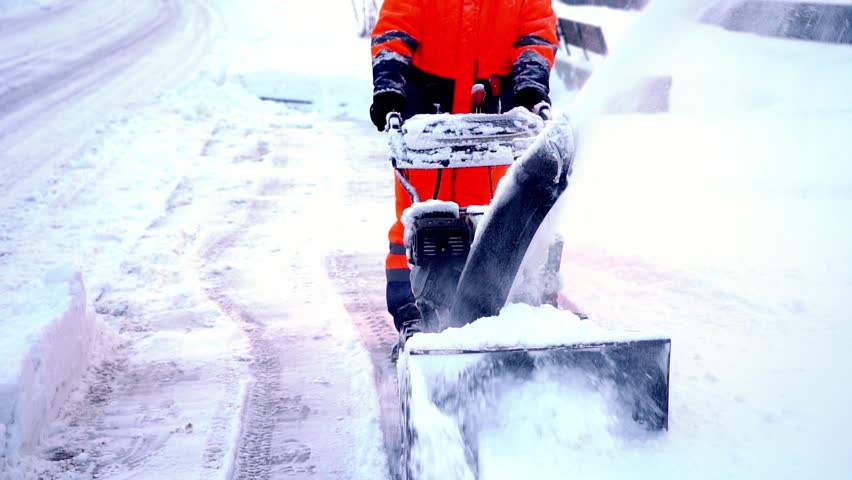 A janitor removes snow after a snowfall on the street with a snow blower