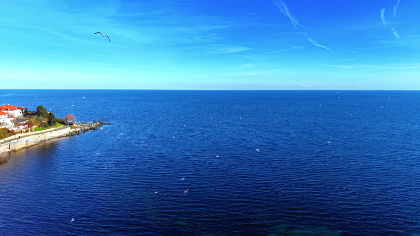 Serene deep blue sea meeting the clear sky, with the rocky edge of the peninsula in the foreground. Black Sea from Nessebar coastline. Aerial view.