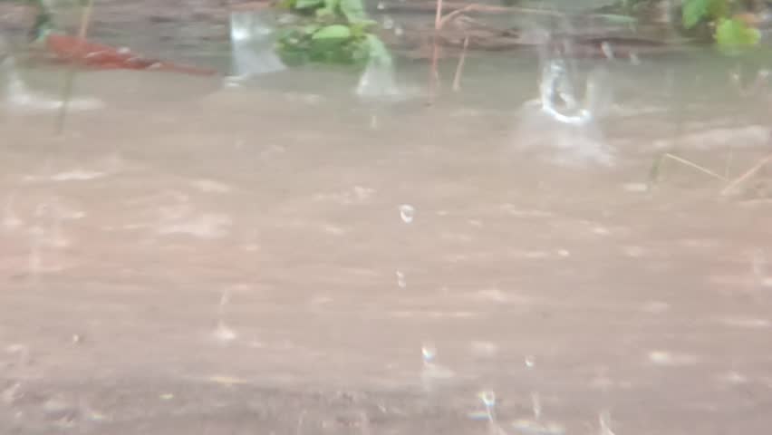Raindrops falling on a water puddle during a heavy rain shower at daytime.