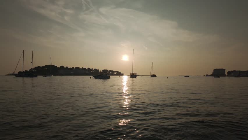 Sunset above the Adriatic Sea. View from the port of Porec, Croatia in golden evening lights. Dreamy scenery of gently rocking boats with calm water surface, tranquil ripples and beautiful reflections