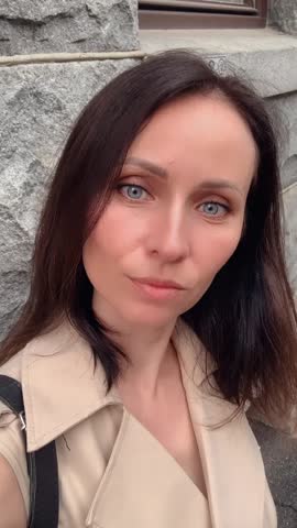 stylish woman with blue eyes and dark hair in beige dress gently shakes her head, gazing into camera against rustic stone wall. Daytime outdoor shoot, exuding natural elegance and mystery. Perfect for fashion brands, beauty ads, stories, or art projects. 9:16 vertical, natural light