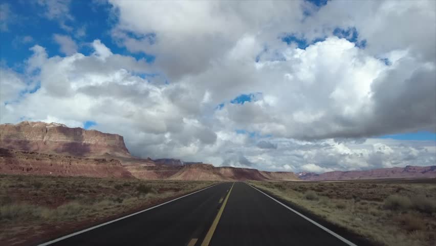 Aerial view of a long road stretching toward mesas under a sky of billowing clouds, creating a stark contrast of earth and sky, Albuquerque, New Mexico, United States.