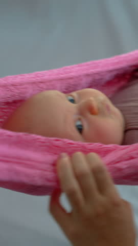 Loving mother gently swings her swaddled two-month-old baby in a hammock to help him fall asleep, creating a peaceful and nurturing family bedtime moment.