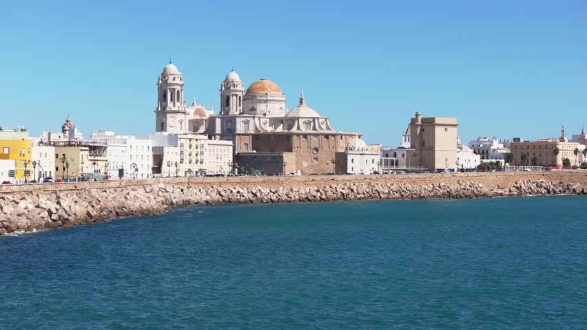 Aerial drone view of Cádiz in Spain, Andalusia, Europe, on bright sunny day, facing Cádiz cathedral and waterfront. Drone flying fast forwards and low, close to water