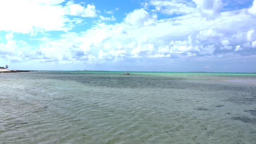 Aerial view of a single boat sailing on the calm, turquoise sea under a partly cloudy sky, creating a serene coastal scene, Nampula, Nampula Province, Mozambique.