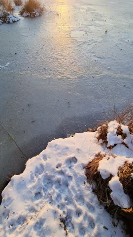 Beautiful golden hour sunset reflecting on the surface of a frozen lake during a cold winter day