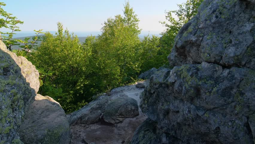A beautiful landscape shot from a rocky viewpoint overlooking dense green forests and rolling hills in the Southern Urals region of Russia on a clear, sunny day.
