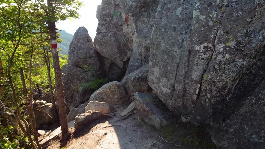Scenic view of a hiking trail winding through large rock formations and green trees in the Southern Urals region of Russia on a sunny day.
