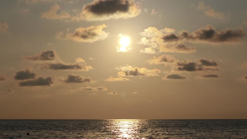 The setting sun casts a radiant glow over the tranquil ocean, casting a stunning reflection on the water. A serene seascape with a dusk sky filled with fluffy clouds
