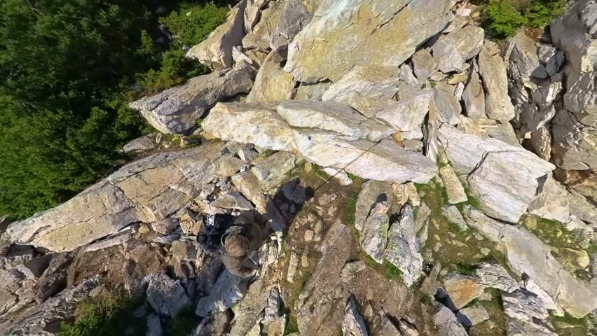 panoramic view from the top of a rugged mountain peak in the Southern Urals, Russia. The natural landscape features large rock formations, dense green forests, and a clear blue sky, highlighting the s