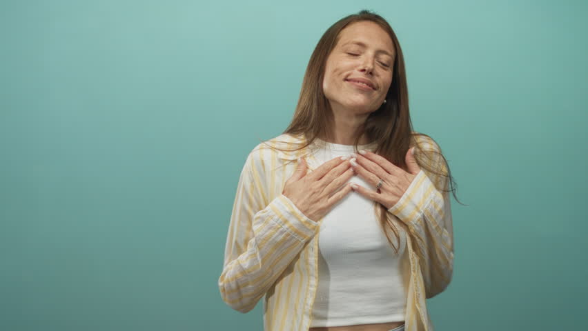 Woman with arms outstretched, hands reaching toward camera in turquoise studio wearing yellow striped shirt and white crop top; joy openness warmth.