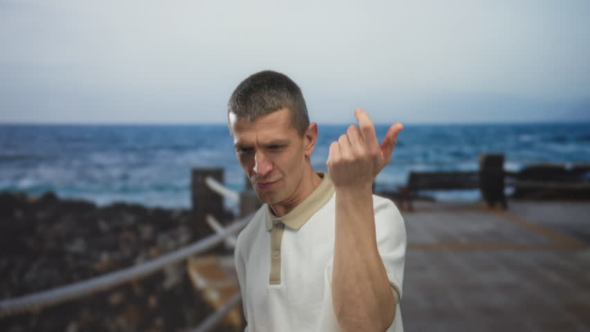 Man joyfully mimicking playing guitar on a seaside promenade, feeling the music with the serene beach and sea as a calming backdrop on a sunny outdoor day.