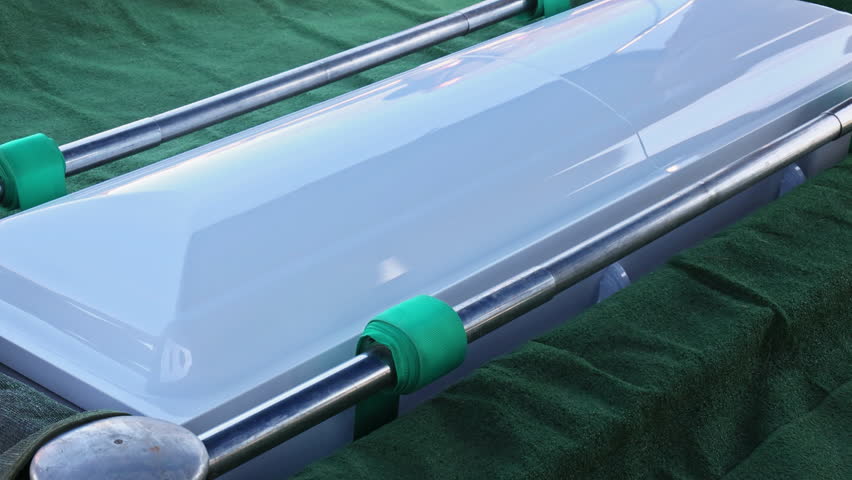 Funeral casket positioned on green drape with metal holders at cemetery service