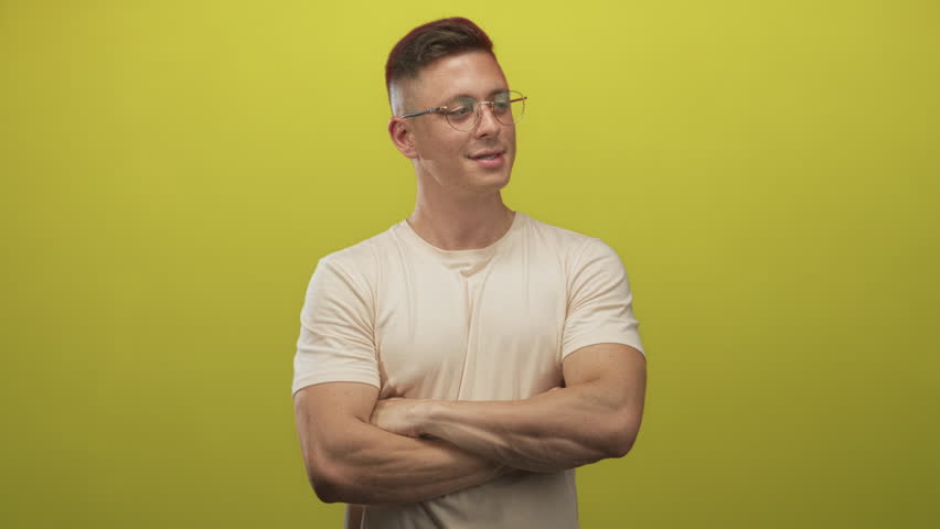Man with arms crossed and visible biceps, wearing round glasses and a t-shirt in studio; confidence.