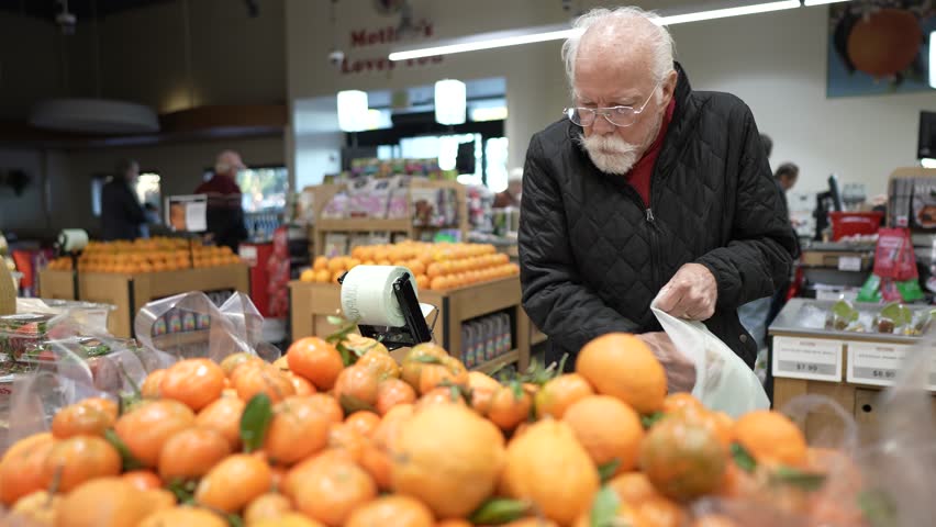 An elderly man is shopping for oranges in a grocery store. He checks the quality of the fruit and places them in his bag.