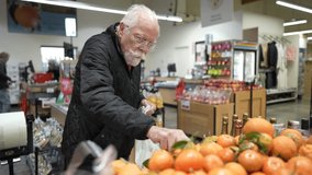 Elderly man selects fruits and vegetables in a grocery store. He carefully places items in a bag while shopping for food. - Powered by Shutterstock - Get 15% off with code: PIKWIZARD15