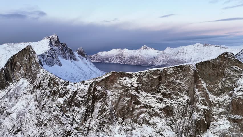 Cinematic drone footage of snow-covered mountains and serene fjord landscape at dusk
