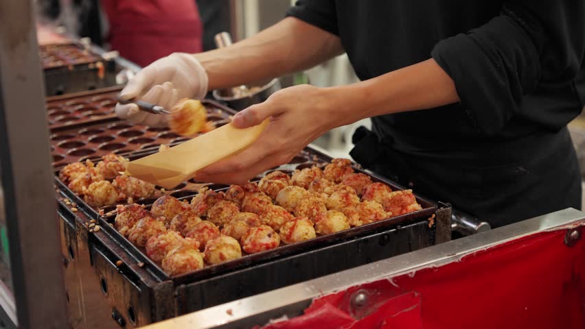 Chef picking up octopus takoyaki, a popular Japanese Osaka street food for tourists