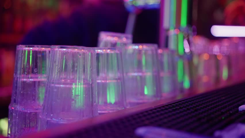 Neonlit Bar With Ready Cups, Colorful Neon Illumination Highlights Organized Rows Of Plastic Cups, Bright Neon Lights Illuminate Neat Stacks Of Transparent Cups Prepared For Lively Celebration