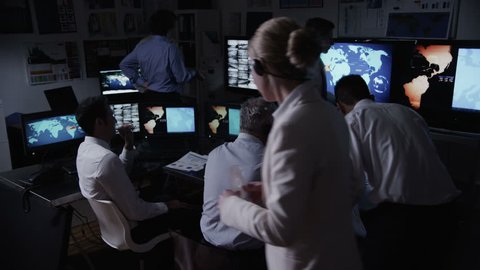 A busy team of security personnel are manning the stations within a busy system control room. 